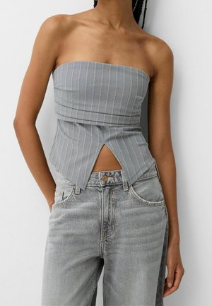 Kobieta ubrana w szary, bezramieniowy top w prążki z przednim rozcięciem, zestawiony z wysokim stanem jasnoszarymi jeansami.