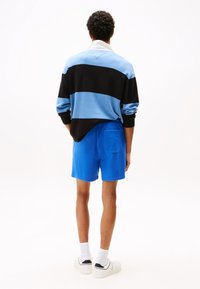 Collared, long-sleeve shirt with blue, black, and light blue horizontal stripes; paired with solid blue shorts and white sneakers.