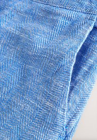 Gros plan sur un tissu bleu plié avec un motif en chevrons détaillé en fils bleu clair et bleu foncé alternés.