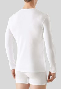 Camicia bianca a maniche lunghe con scollo rotondo e design aderente, abbinata a pantaloni corti bianchi. Tessuto morbido, cuciture minime, styling semplice.