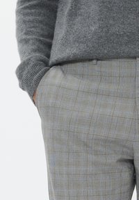 Suéter de lana gris con puños acanalados, usado sobre pantalones cuadros gris claro con finas líneas azules y marrones. Ajuste entallado, textura suave.
