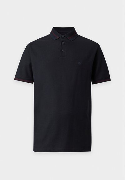 Polo noir à manches courtes avec trois boutons et coutures rouges discrètes sur le col et les poignets, présenté sur fond blanc.
