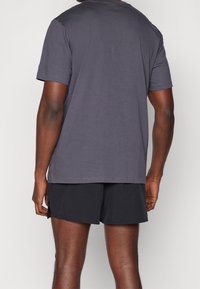 Camiseta de algodón gris con un corte relajado, mangas cortas y escote redondo, combinada con pantalones cortos deportivos negros. Sin logotipos visibles.