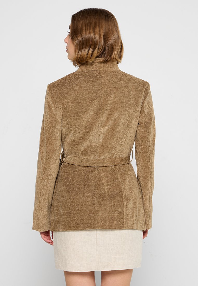 Blazer in corduroy marrone con un design aderente, maniche lunghe e vita con cintura. Texture liscia, semplice, senza motivi o decorazioni.