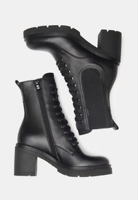 Les bottes noires en cuir à lacets présentent un talon empilé, un laçage frontal, une fermeture éclair latérale et un panneau élastique, avec un dessus texturé et une semelle robuste.