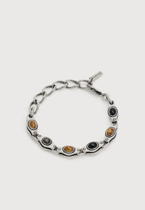 Bracciale a catena argentata con pietre ovali alternate nere e marroni e una piccola targhetta Versace vicino alla chiusura.