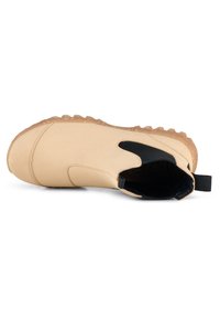 Beige slip-on stövel med en texturerad gummisul, elastiska sidopaneler och en dragflik vid hälen för enkel på- och avtagning.