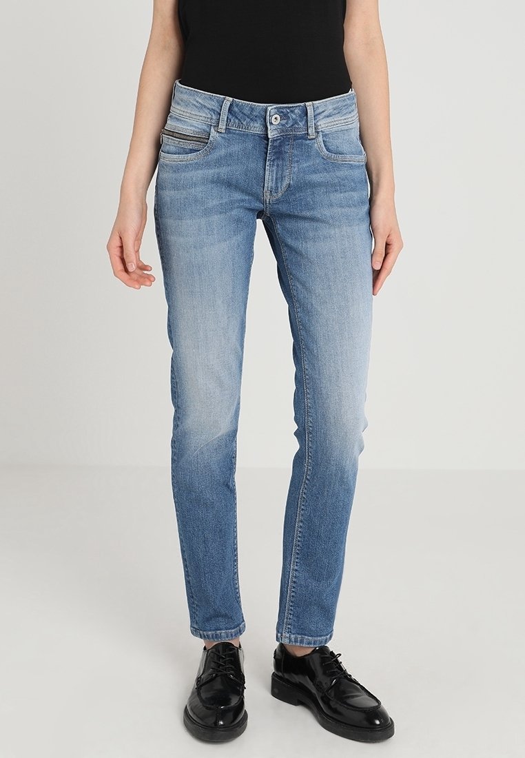 Světle modré džínové kalhoty s vybledlým efektem, úzkým střihem, pěti kapsami a jemnými švovými detaily. Nošeny s černou obuví.