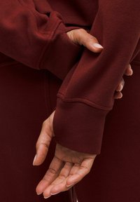 Felpa bordeaux con maniche lunghe, polsini a costine e dettagli di cucitura, abbinata a pantaloni coordinati; mani posizionate dietro la schiena.