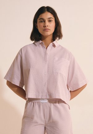Donna che indossa una camicia a righe larga, a maniche corte con bottoni e pantaloni coordinati con vita elastica con etichetta "Week End Club."