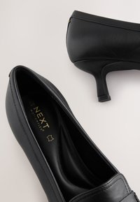 Chaussures à talons hauts noires en cuir lisse, dotées d'un bout rond, d'un design profilé bas et de détails dorés à l'arrière.