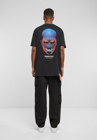 Black t-shirt with a colorful graphic of a face and butterfly on the back. Paired with loose-fitting black cargo pants and white sneakers.