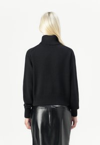 Pull à col roulé court noir avec poignets et ourlet côtelés, texture tricotée, assorti à une jupe en cuir noire taille haute.