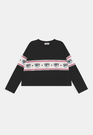 Haut noir à manches longues avec une bande horizontale blanche ornée d'yeux bleus avec cils et d'étoiles noires, bordée de lignes roses et argentées.