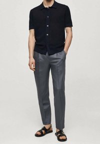 Námořnická košile s krátkým rukávem a knoflíky, šedé kalhoty na míru a černé sandály. Strukturovaná tkanina, slim fit a klasický design límce.