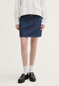 Mørkeblå denimskjørt med to frontlommer, rett snitt og kontrasterende sømmer. Kombinert med svarte loafers og hvite sokker.