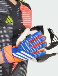 Blaue und orange Torwarthandschuhe mit texturiertem Griff und weißen Akzenten, gehalten neben einem schwarz-weißen Fußball mit einem Logo.