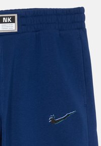 Marina blå sweatpants i mjukt tyg, med elastisk midjeband och en liten svart och blå Nike-logotyp på vänster sida.