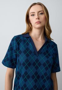 Polo a maniche corte blu navy con scollo a V, caratterizzato da un motivo a diamante in tonalità di blu e verde, colletto a costine e tessuto texture.