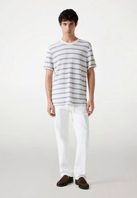 Gestreiftes T-Shirt in Weiß und Hellblau, kurzärmlig, mit gerippter Struktur. Kombiniert mit weißen Hosen und braunen Slippern.