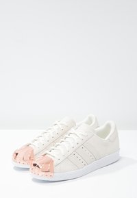 Vita lädersneakers med en texturerad yta, med en metallisk roséguldkappa och vit gummisula.