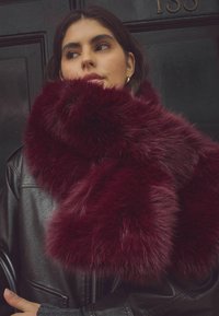 Bordeaux faux fur sjaal met een zachte, fluffy textuur, gewikkeld om de hals en contrasterend met een zwarte leren jas.