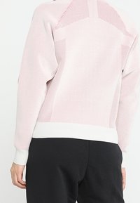 Suéter de punto de color rosa claro con paneles de malla texturizados y puños acanalados en blanco. Corte casual, la vista trasera muestra detalles de diseño en los hombros.
