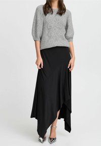 Grå stickad tröja med ett texturerat mönster, kombinerad med en svart asymmetrisk maxikjol. Silvriga klackar med spetsig tå fulländar looken.