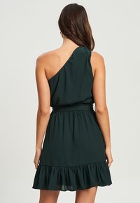 Zielona, jednoskładnikowa sukienka z miękkiego materiału, z dopasowanym paskiem i falbaną na dolnej krawędzi, z teksturowaną powierzchnią i czystymi liniami.