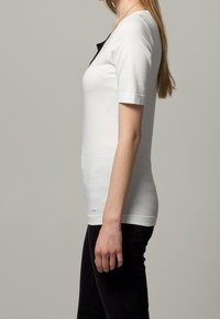 Hvid kortærmet t-shirt med rund halsudskæring, der har en kontrasterende sort detalje ved kraven, lavet af blødt bomuldsstof.
