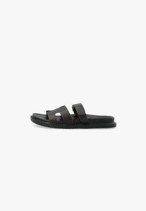 Üksik tumedat pruunist nahast libisev sandaal kahe laia rihmaga ja lameda musta taldiga valgel taustal.