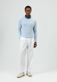 Lichtblauwe ribgebreide trui, witte linnen broek en beige sneakers. Voorzien van een ronde hals en een sjaal met patroon rond de nek.