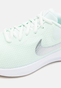 Basket en maille vert clair avec des lacets blancs, une semelle blanche et un accent logo argenté sur le côté, featuring une surface texturée.