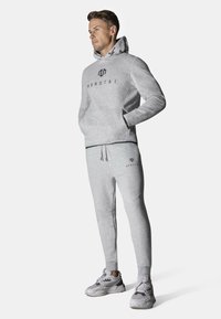 Grå hettegenser og matchende joggebukser laget av mykt materiale. Har en logo på brystet og buksen. Utsmykket med snor og ribbestrikkede mansjetter.