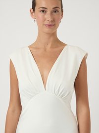 Λευκό φόρεμα με βαθύ V-λαιμόκοψη, κοντά μανίκια και λεπτομέρεια πτυχώσεων στη μέση. Λείο ύφασμα με απαλό ύφος και εφαρμοστή σιλουέτα.