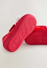 Punaiset pehmeät kangassandaalit, joissa on valkoisia pom-pom-yksityiskohtia. Teksturoitu kumipohja, jossa on soikeat pito-kuviot. Koko "6" ja "next"-brändäys sivussa.