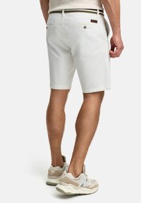 White cotton shorts with a back pocket, complemented by a brown leather label. Worn with light gray sneakers featuring beige accents.