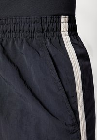Sorte idrettsshorts med en teksturert finish, med elastisk midjebånd og en hvit sidestripe langs sømmen. Lett materiale.