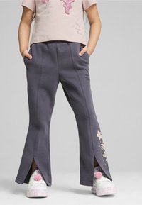 Grå sweatpants med sideskår og blomstermotiver, lavet af blødt stof. Kombineret med hvide sneakers med pink detaljer.