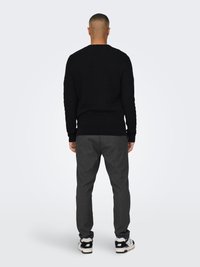 Black textured knit sweater with a crew neck, paired with gray pinstripe trousers and black sneakers with white accents.