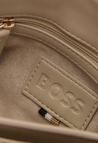 Interno in pelle beige con superficie texturizzata, caratterizzato da una chiusura a zip e un'etichetta con il marchio impresso con "BOSS". Dettagli di cucitura sottili inclusi.