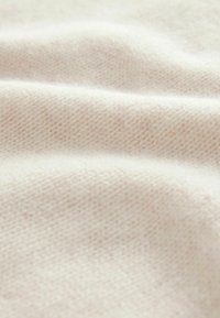 Tela de cachemira color beige claro con una textura suave, que presenta un sutil patrón de punto y suaves ondas.
