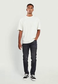 Άσπρο βαμβακερό μπλουζάκι με κοντά μανίκια, συνδυασμένο με σκούρες τζιν παντελόνες. Μαύρα και άσπρα αθλητικά με κορδόνια και αντιθετικά σχεδιαστικά στοιχεία.