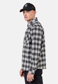 Zwart-wit geruite flanellen shirt met een knoopsluiting, lange mouwen en een borstzak, met een gladde textuur.