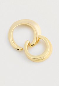 Dos aretes en forma de aro de oro entrelazados con superficies lisas y pulidas reposando sobre un fondo blanco.