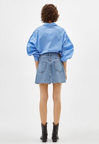 Blå randig oversized skjorta med puffärmar, som matchas med en denim minikjol med fransar. Svarta ankelstövlar fulländar outfiten.