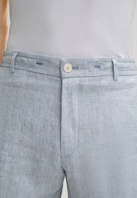 Jasnoniebieskie spodnie w kratkę charakteryzują się teksturowanym materiałem, standardowym zapięciem na guzik oraz szlufkami na pasek, a także subtelnym wzorem w kratkę.