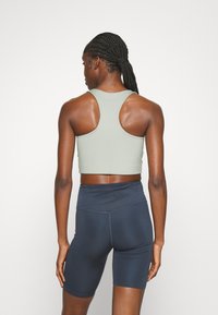 Sportski crop top u svijetlozelenoj boji s dizajnom na leđa, uparen s tamnoplavim biciklističkim šortsevima visokog struka. Glatka, rastezljiva tkanina, bez uzoraka.