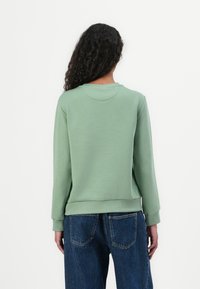 Felpa verde con collo rotondo, orlo a costine e maniche lunghe. Lo stile è rilassato, con una texture liscia e senza grafiche visibili.