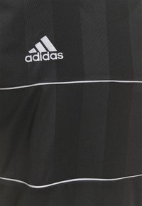 Camiseta deportiva negra con rayas verticales texturizadas, logo de Adidas en blanco y una línea horizontal blanca cerca de la parte inferior.